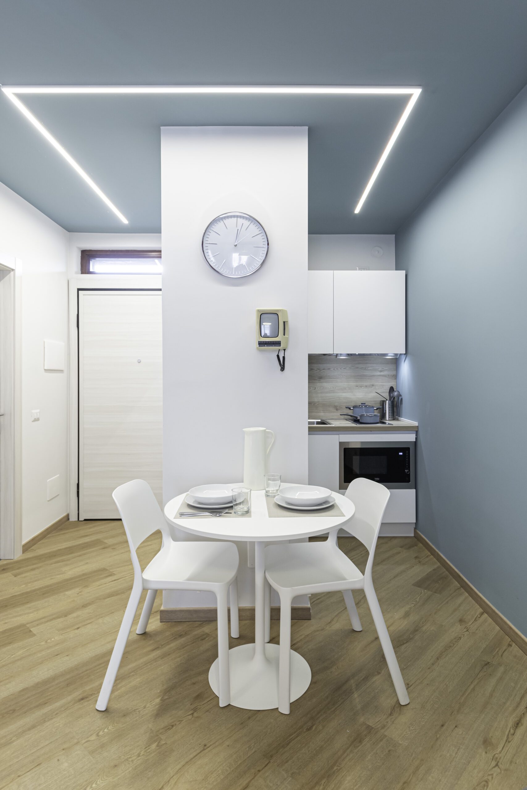 Zona living_ottanio Open space luminoso nei toni dell'azzurro e ottanio, con una piccola cucina bianca integrata e un elegante tavolo da pranzo rotondo